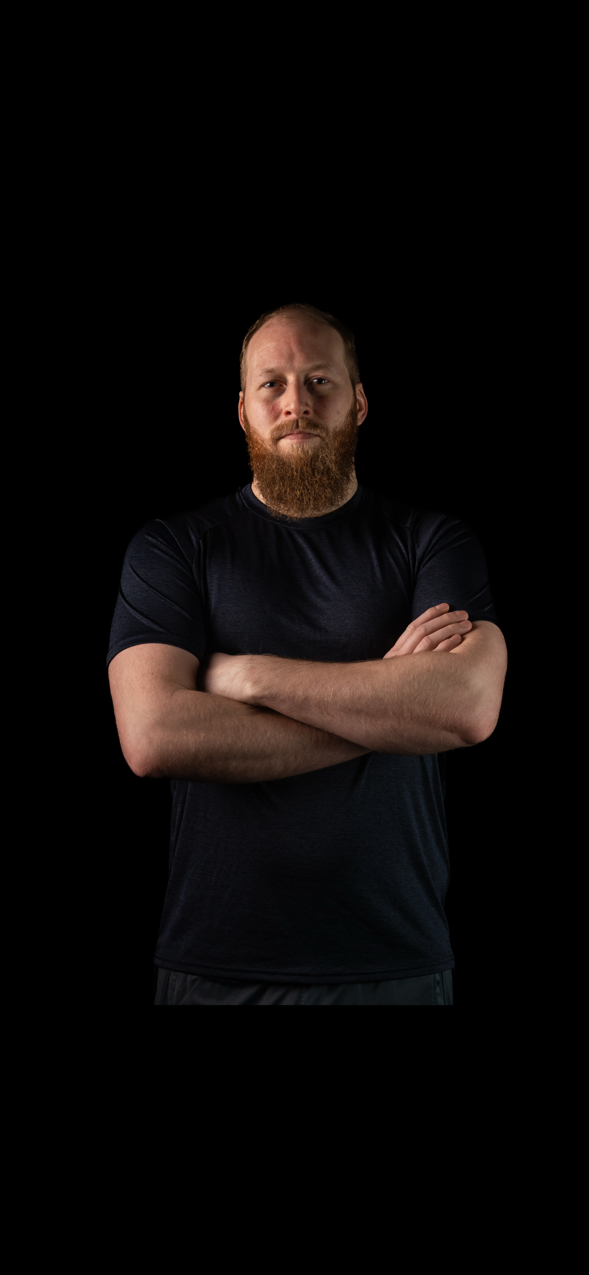 Man with a beard wearing a black t-shirt against a black background